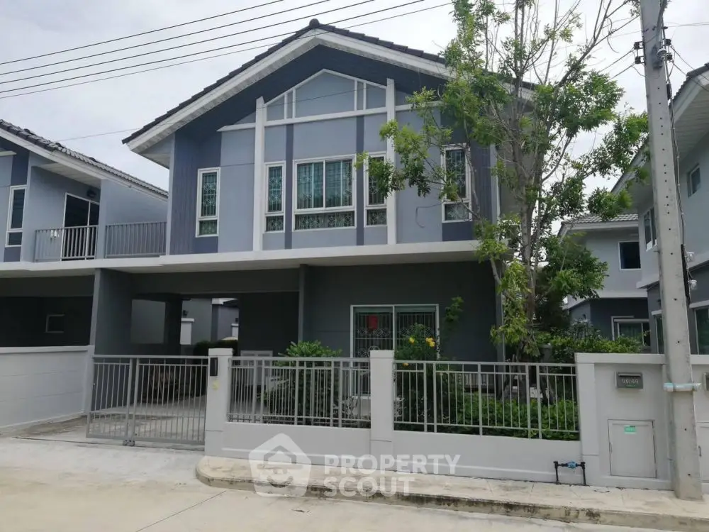 Modern two-story house with a gated driveway and lush greenery in a suburban neighborhood.