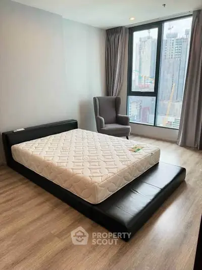 Modern bedroom with city view, featuring a stylish bed and cozy armchair, perfect for urban living.