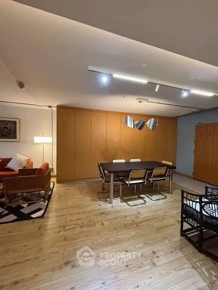 Spacious living room with modern dining area and stylish lighting, featuring wooden flooring and cozy seating.