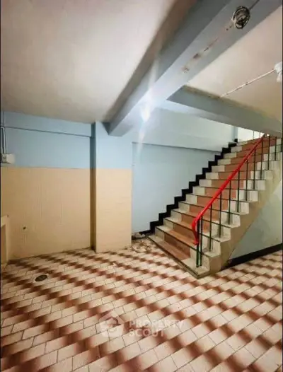 Spacious stairwell with tiled flooring and red railing in a residential building.