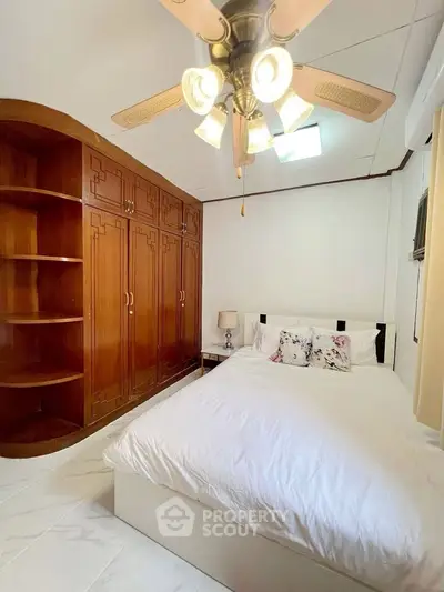 Cozy bedroom with wooden built-in wardrobe and ceiling fan, perfect for relaxation.