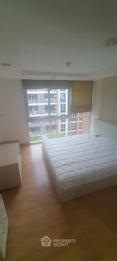 Spacious bedroom with large window offering city view and natural light