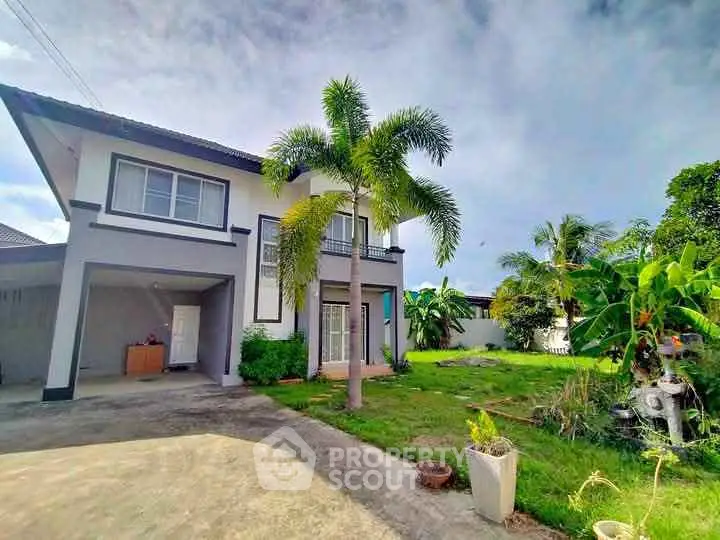 Charming two-story house with lush garden and driveway in tropical setting.