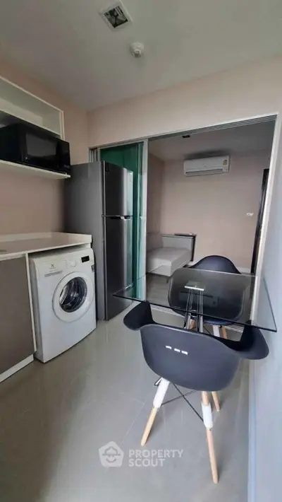 Modern kitchen with glass dining table, washing machine, and sleek appliances in a compact open layout.