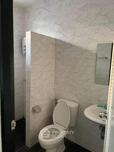Compact bathroom with tiled walls, toilet, sink, and shower area, ideal for efficient space use.