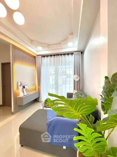Modern living room with stylish lighting and large window, featuring cozy seating and lush indoor plants.