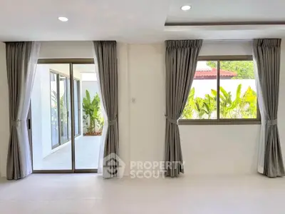 Spacious living room with large windows and sliding doors opening to a lush garden view.