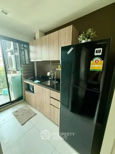 Modern kitchen with sleek black fridge and wooden cabinets, featuring a compact open layout.