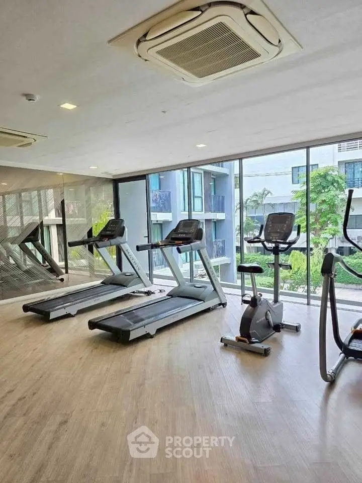 Modern gym with treadmills and exercise bike in a bright, glass-walled room overlooking greenery.