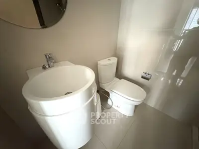 Modern bathroom with sleek fixtures and minimalist design, featuring a compact sink and toilet.