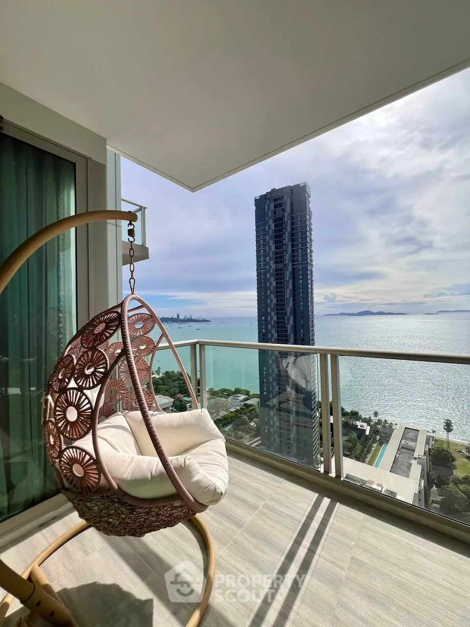 Stunning balcony view with modern swing chair overlooking ocean and city skyline.