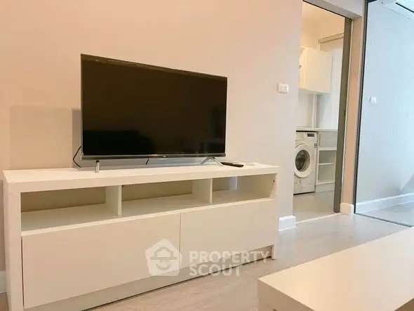 Modern living room with sleek TV stand and view into kitchen with washing machine.