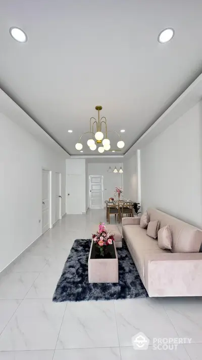 Elegant spacious living room with glossy white tiles, plush sofa, and modern chandelier, seamlessly connecting to a cozy dining area.