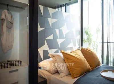 Modern bedroom with geometric accent wall and large windows offering natural light.