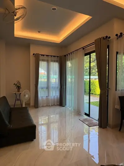 Spacious living room with elegant lighting and large windows overlooking a lush garden.