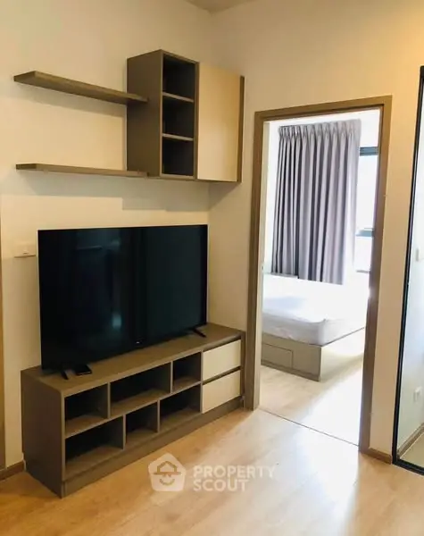 Modern living room with sleek TV unit and view into cozy bedroom