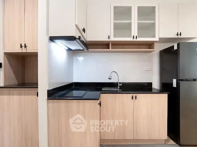 Modern kitchen with sleek black countertops and wooden cabinetry, featuring a built-in stove and spacious fridge.