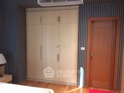 Modern bedroom with built-in wardrobe and wooden door, featuring stylish striped wallpaper.