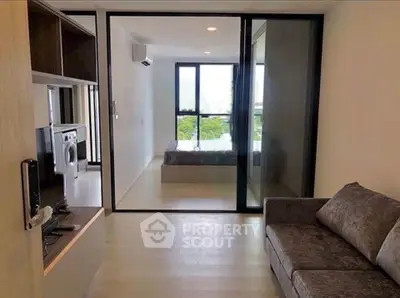 Modern apartment interior with open living room and bedroom view, featuring sleek furniture and natural light.