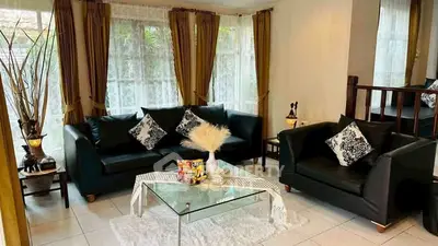 Elegant living room with black sofas, glass coffee table, and large windows with curtains.