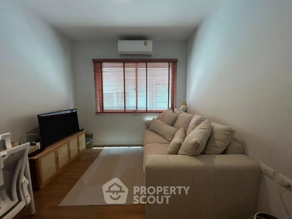Cozy living room with modern sofa and TV, featuring natural light from window blinds.