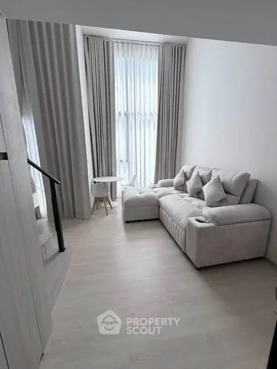 Modern living room with high ceilings, large windows, and elegant gray sofa in a stylish apartment.