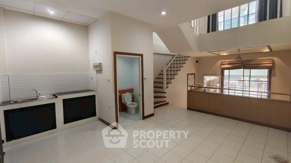Spacious open-plan living area with kitchen and staircase, featuring natural light and modern design.