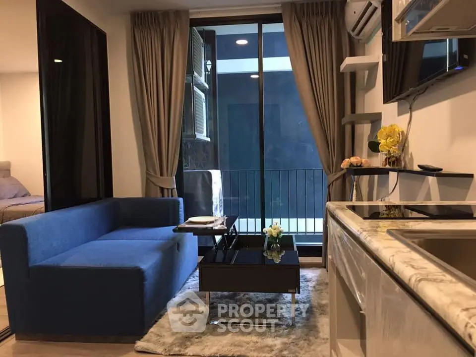 Modern living room with blue sofa, glass coffee table, and balcony view in stylish apartment.