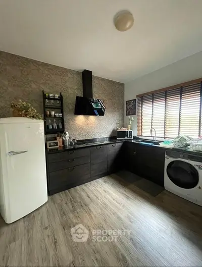 Modern kitchen with dark cabinetry, vintage fridge, and washing machine, featuring open layout and stylish decor.