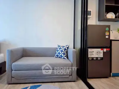 Modern living room with stylish gray sofa and sleek kitchen area featuring a compact refrigerator.
