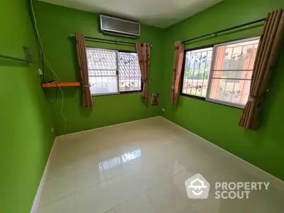 Vibrant green-walled room with gleaming tiled floors, ample natural light, and air conditioning unit, perfect for a cozy living space.