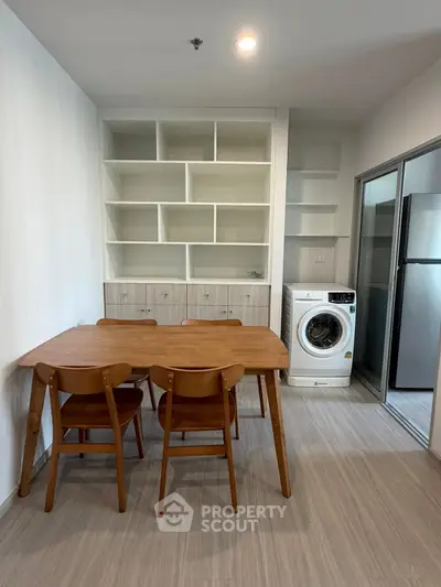 Modern dining area with wooden table, chairs, and built-in shelves, adjacent to a compact laundry space.