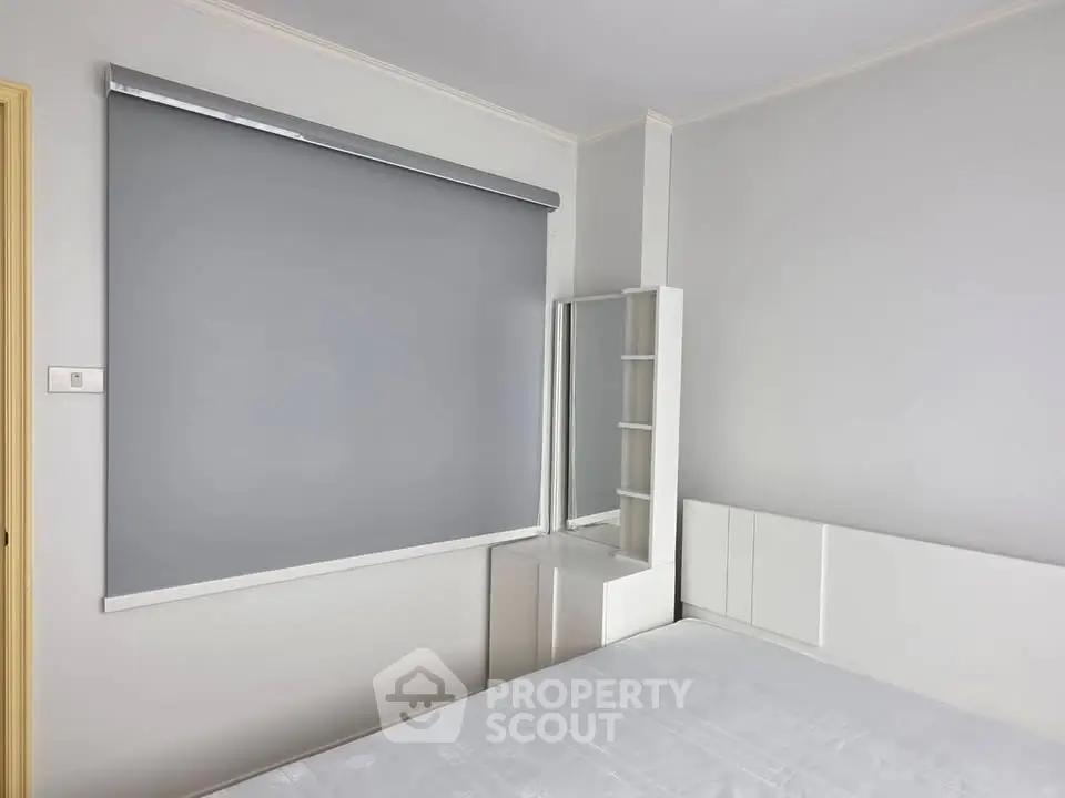 Modern minimalist bedroom with sleek white furniture and large window shade.