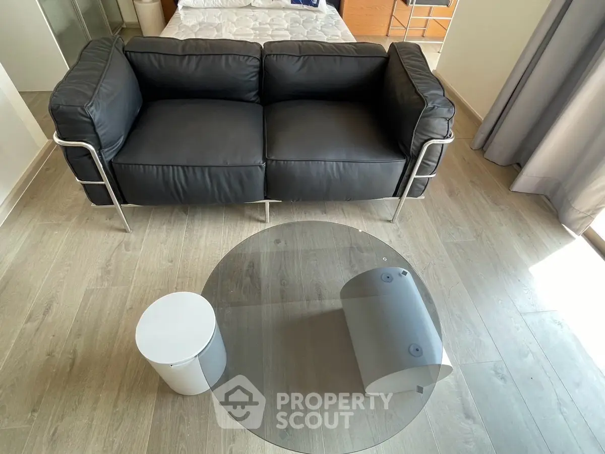 Modern living room with sleek black sofa and stylish glass coffee table on wooden flooring.