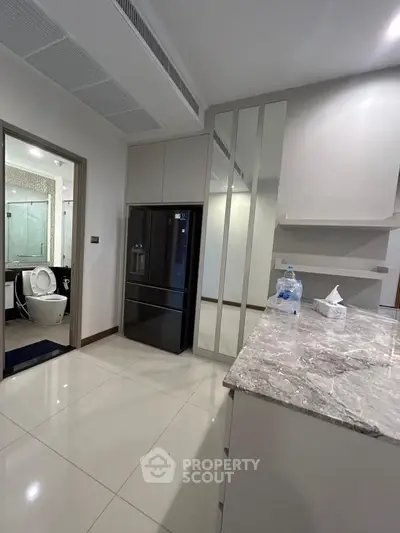 Modern kitchen with sleek design and marble countertop, adjacent to a bathroom with glass shower.