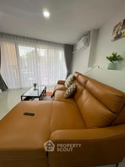 Spacious living room with leather sofa and large windows offering natural light