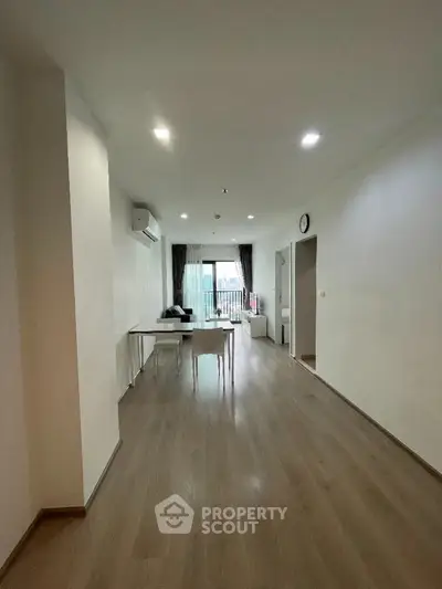 Spacious modern living room with wooden flooring and natural light, featuring a dining area and balcony access.