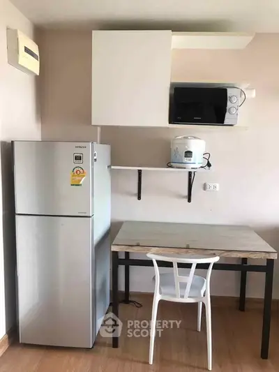 Compact kitchen with fridge, microwave, and dining table in modern apartment.