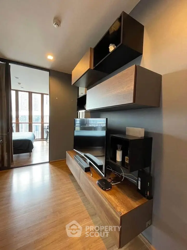 Modern living room with sleek wooden shelves and TV, leading to a cozy bedroom with balcony view.