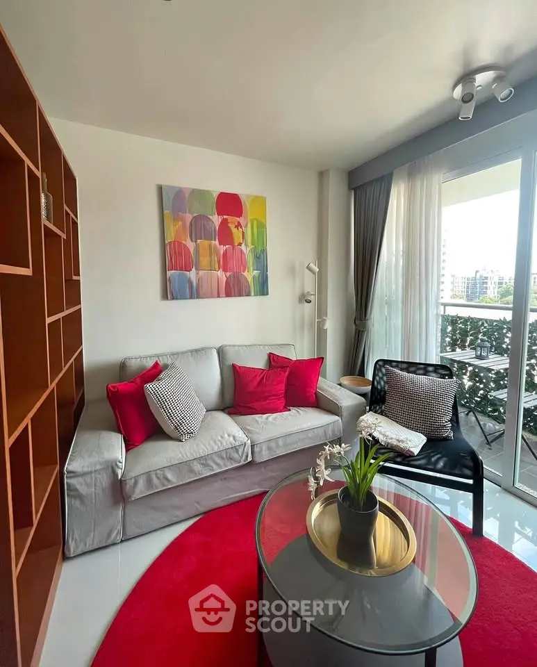 Chic living room with modern decor, vibrant red accents, and a cozy balcony view.