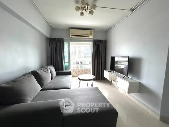 Modern living room with gray sectional sofa, TV, and air conditioning, featuring large window for natural light.