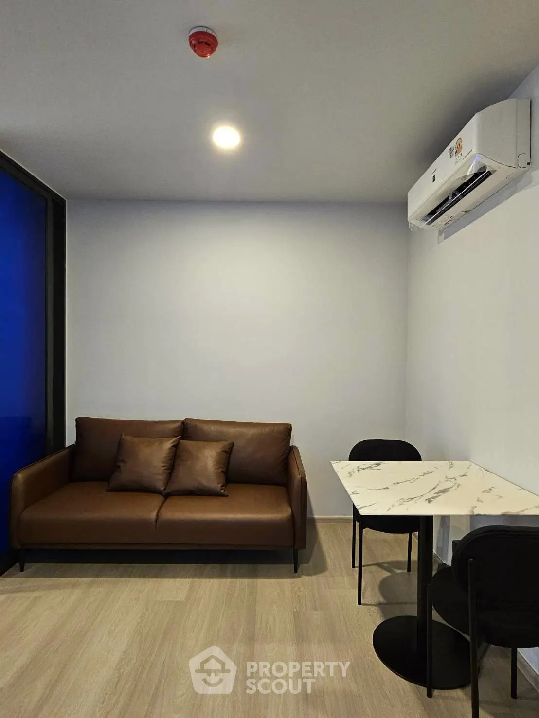 Modern living room with sleek brown sofa and marble dining table, featuring air conditioning and stylish decor.