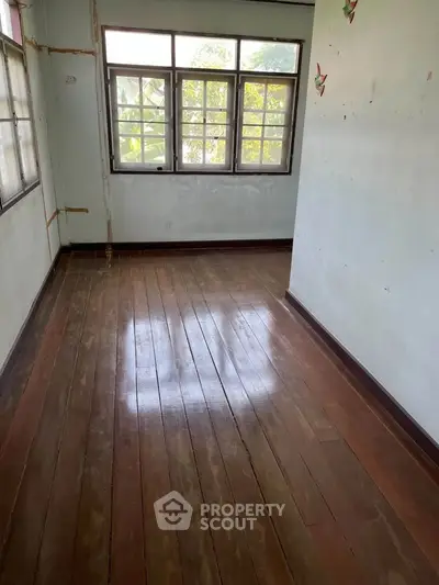 Spacious room with wooden flooring and large windows offering natural light.