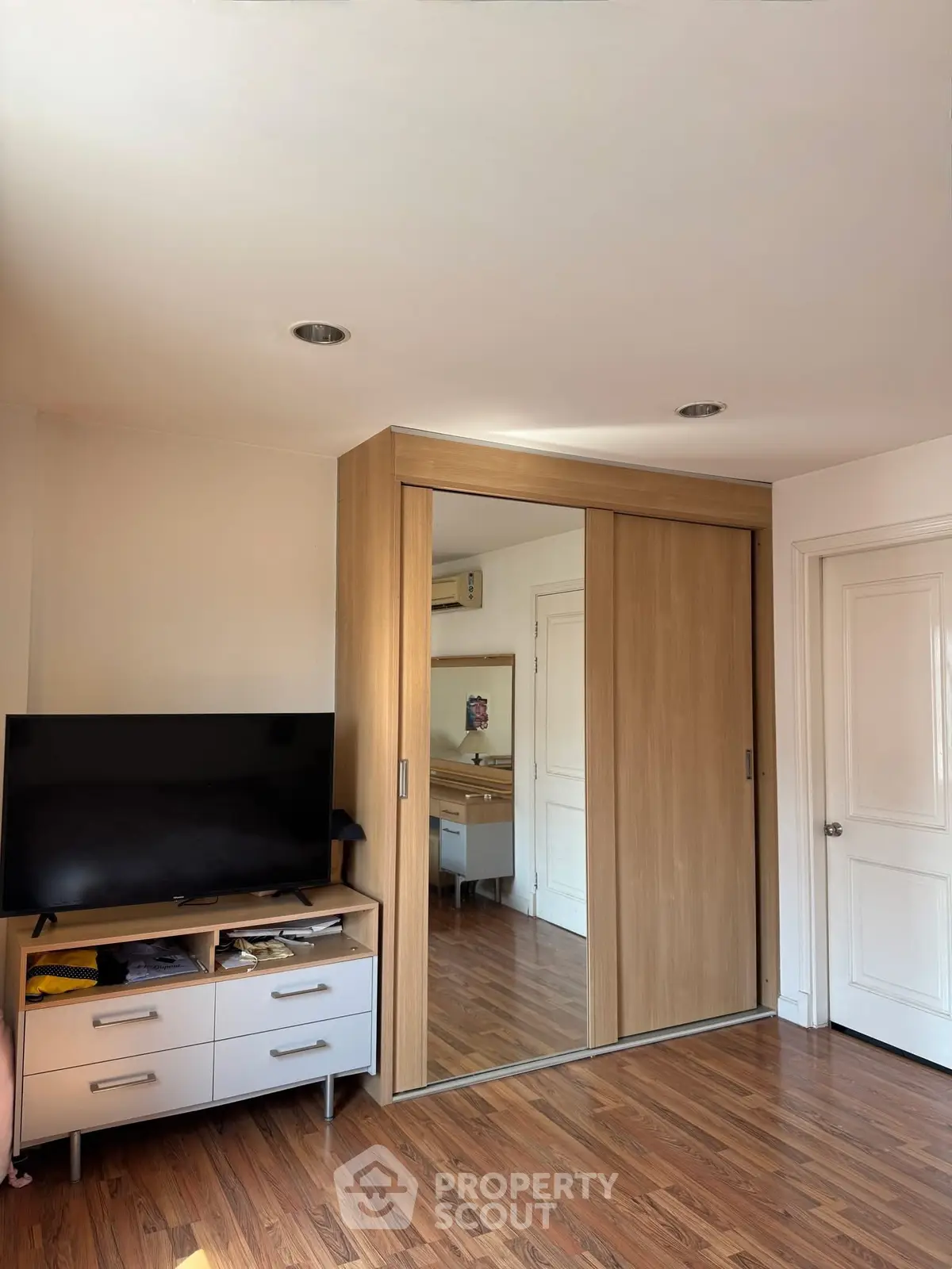 Modern bedroom with mirrored wardrobe and sleek TV stand on wooden flooring.