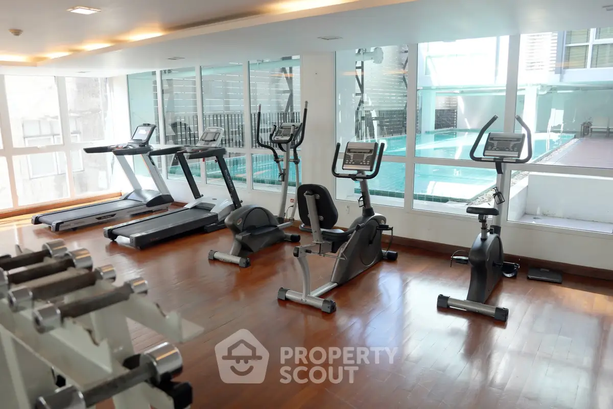 Modern gym with pool view featuring exercise bikes and treadmills in a luxury apartment complex.