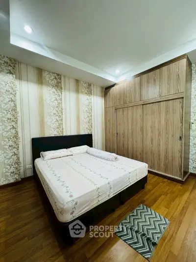 Cozy bedroom with wooden flooring and stylish wallpaper, featuring a comfortable bed and spacious wardrobe.