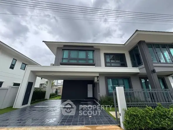 Modern two-story house with sleek design and spacious driveway under cloudy sky.