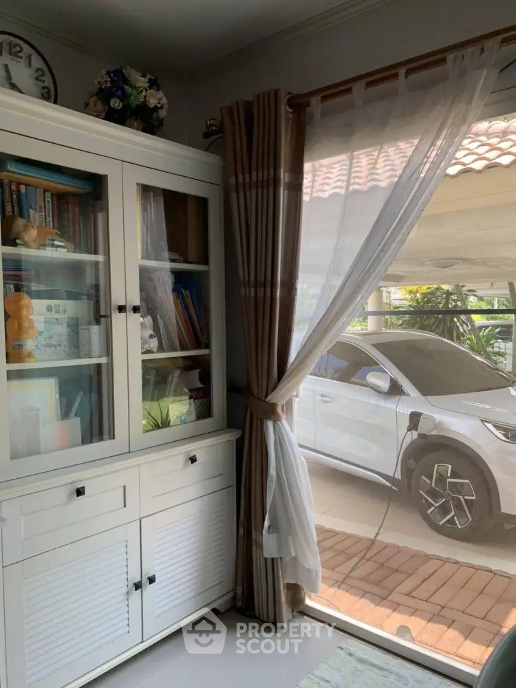 Cozy study room with elegant cabinet and view of parked car outside window.