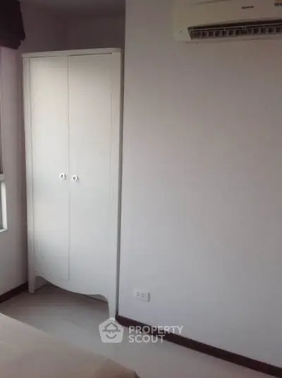Minimalist bedroom with white wardrobe and air conditioning unit.