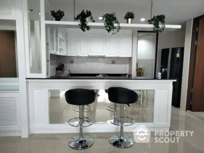 Modern kitchen with white cabinetry and sleek bar stools, complemented by stainless steel appliances and elegant lighting.